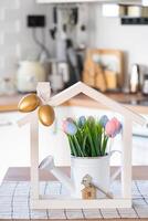 Key and tiny house of cozy home with Easter decor with color eggs on table of kitchen. Building, design, project, moving to new house, mortgage, insurance, rent and purchase real estate photo