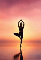 ai generado silueta de joven mujer practicando yoga en el playa a puesta de sol. ai generativo foto