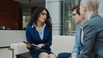 Businesswoman in glasses talking and duscussing future contract with business partners sitting on couch in modern office indoors photo