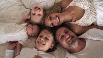 A family of five lies on the bed and laughs while looking at the camera. View from above. video