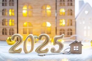 Golden figures number 2025, key and tiny home on background of cozy windows of a house with warm light with festive decor of stars,snow and garlands. Greeting card, Happy New Year, cozy home photo