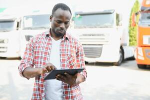 Front view. Young african truck driver is with his vehicle at daytime. photo