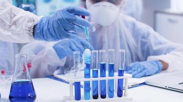 Female scientist taking notes and looking at smoking blue fluid. Scientist colleague adding solution with pipette. video