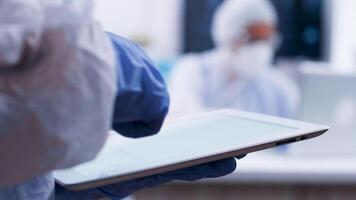 Chemical scientist working in a modern laboratory typing formula on tablet. Team of scientist working in the background video