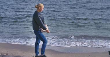 une fille dans jeans des promenades le long de le noir mer digue sur une ensoleillé journée. anamorphique video