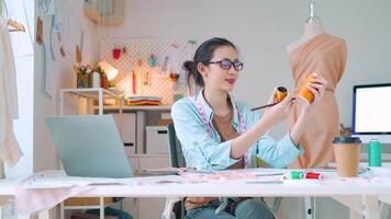 een gelukkig vrouw ondernemer in haar studio is maken nieuw kleding collecties van haar ontwerp. video