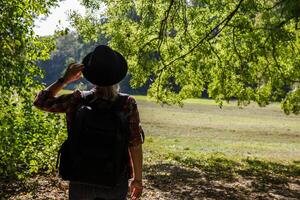 young caucasian woman with a backpack and hat in the shade of trees near the field. Background, close up. Selective focus.background blurred.High quality photo