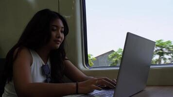 indonesio joven mujer de negocios es sentado abajo en un tren haciendo algunos trabajo mediante su ordenador portátil video