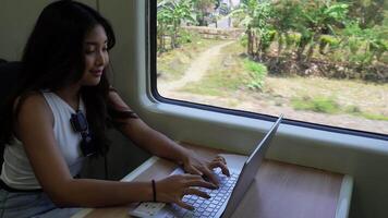 indonesio joven mujer de negocios es sentado abajo en un tren haciendo algunos trabajo mediante su ordenador portátil video