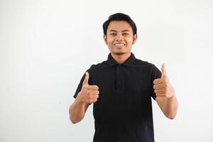 contento o sonriente joven asiático hombre dando dos pulgares arriba vistiendo negro polo t camisa aislado en blanco antecedentes foto