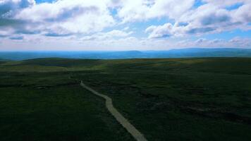 Scenic aerial view of a winding trail through vast green moorland under a cloudy sky. video