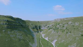 aéreo ver de un lozano verde Valle con un serpenteante río, rodeado por rocoso acantilados debajo un claro azul cielo. video