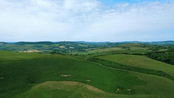 aéreo Visão do exuberante verde rolando colinas com agrícola Campos debaixo uma nublado céu. video