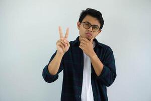 young asian man showing curious face expression while giving two fingers sign isolated on white background photo