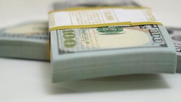 stack of bank bundles with US dollars on a white background. Close-up shot of new, freshly printed hundred-dollar bills rotating on a table. cash flow, business investment, or big money concepts. video