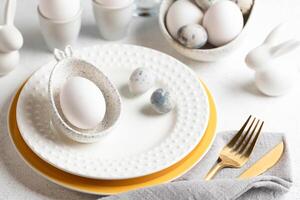 Easter table. Festive elegant white with yellow table setting with eggs, plates, golden cutlery. photo