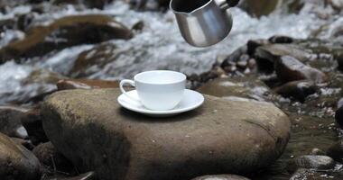 café est versé dans une tasse de une café fabricant. petit déjeuner sur le banque de une magnifique rivière. Voyage concept. 4k video