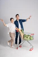 Image of Asian couple pushing supermarket cart while shopping, isolated on white background photo