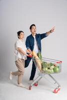 Image of Asian couple pushing supermarket cart while shopping, isolated on white background photo