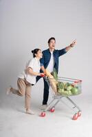 Image of Asian couple pushing supermarket cart while shopping, isolated on white background photo