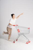 sonriente mujer felizmente emprendedor un supermercado carro, aislado en blanco antecedentes foto