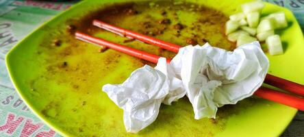 Close up view of a photo of the plate after eating, you can see several dirty tissue sheets and a pair of eating used chopsticks.