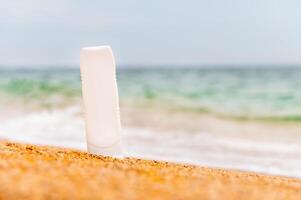 un botella de protector solar sin un etiqueta en el playa en un soleado día. blanco para publicidad tu crema y etiquetas foto