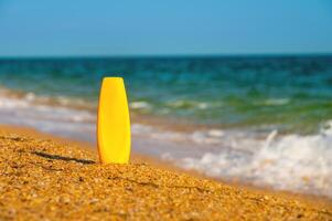 un botella de protector solar sin un etiqueta en el playa en un soleado día. blanco para publicidad tu crema y etiquetas foto