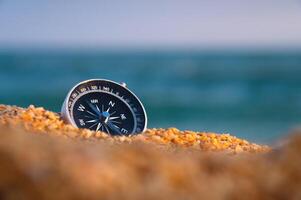 Conceptual photo of a compass in coarse sand against the background of the sea and sky, close-up, without people