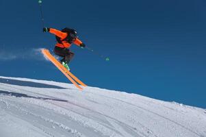 A skier in an orange jacket and a black helmet makes a jump on a sunny day against a clear sky. Copy space for your information photo