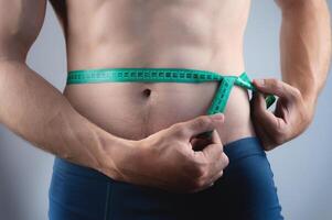 Close-up of the bare torso and waist area with a measuring tape. A man of average build controls his belly size photo