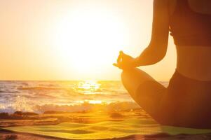 de cerca yoga mujer meditando a sereno puesta de sol o amanecer en el playa. el niña relaja en el loto posición. dedos doblada en mudras. foto