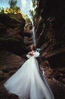 Pareja en amor en contra el fondo de un cascada. Luna de miel viaje. contento Pareja en el montañas. vertical foto de recién casados abrazando en contra el fondo de un cascada en el garganta