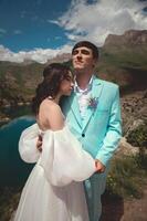 beautiful wedding couple hugs tenderly against the backdrop of a mountain river and lake, the bride's long white dress photo