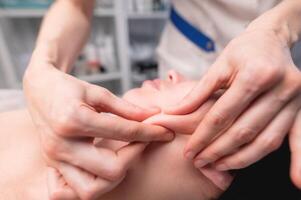 cosmético facial masaje procedimiento. de cerca de el cara de un joven mujer acostado en su atrás, haciendo un cara levantamiento masaje, ratería y laminación técnica foto