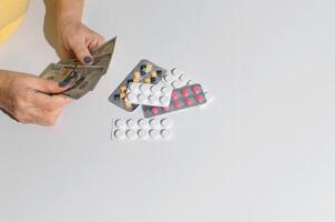 Elderly woman's hands holding money. Tablets on white table top view, copy space. Concept of treatment cost, medicine price, health insurance budget photo