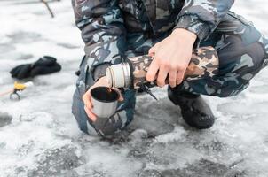 Male hand pouring tea from a thermos, outdoors in winter. photo