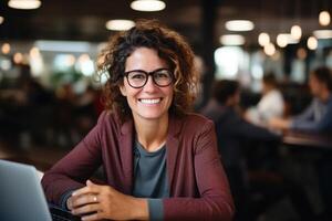 AI generated Positive middle aged businesswoman using laptop while working in coworking space, smiling lady in glasses sitting at table indoors and looking at camera photo