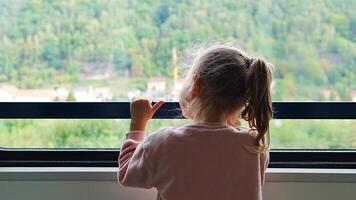 hermosa pequeño niña mirando fuera tren ventana afuera, durante Moviente. de viaje por ferrocarril en Europa. alto calidad 4k imágenes video