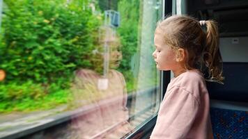 Bored little girl looking out train window outside, during moving. Traveling by railway in Europe. High quality 4k footage video