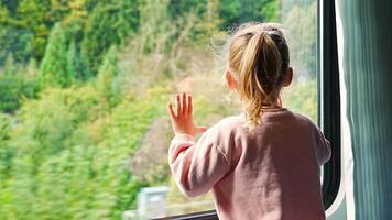 poco ragazza guardare su treno finestra fuori, durante in movimento. in viaggio di ferrovia, Europa. alto qualità 4k metraggio video