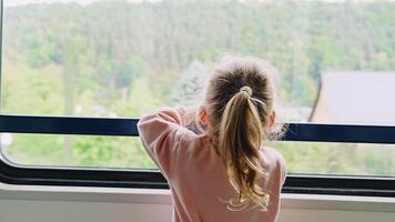 Beautiful little girl looking out train window outside, during moving. Traveling by railway, Europe. High quality 4k footage video