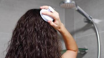 ung kvinna med mörk lockigt hår håller på med själv hår skalp massage med skalp massager eller hår borsta för hår tillväxt stimulerande på Hem badrum. hög kvalitet 4k antal fot video
