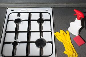 Dirty gas stove surface, yellow gloves and a washing sponge and cleaning agent. Household hygiene concept. photo