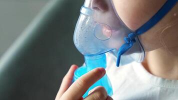 cerca arriba ver de pequeño niña son sentado y participación un nebulizador máscara propensión en contra el rostro, vías respiratorias tratamiento concepto. alto calidad 4k imágenes video