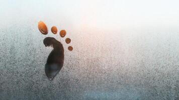 Drawing of a child's foot on a frozen window, copy space. Frosty pattern on glass. Funny creative concept. Textured ice surface. photo