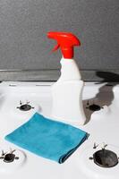 Cleaning supplies for washing the house. Rag and chemical liquid spray standing on the surface of a gas stove. photo