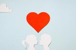 San Valentín día concepto. besos niña y chico siluetas creativo amor tarjeta. rojo corazón y nubes en un pastel azul antecedentes. plano poner, parte superior vista. foto
