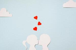 Valentine's Day concept. Cardboard silhouettes girl and boy kissing. Creative love card. Red hearts, clouds on a pastel blue background. Flat lay, top view. photo