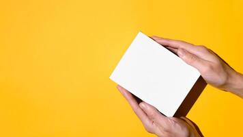 Male hands holding a box on a yellow background, flat lay. Empty white box mock up. Top view, copy space. Delivery concept, gift box. photo